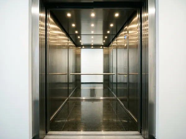 Refurbished passenger lift cab interior with brushed stainless walls, walnut detail and mirrored back panel