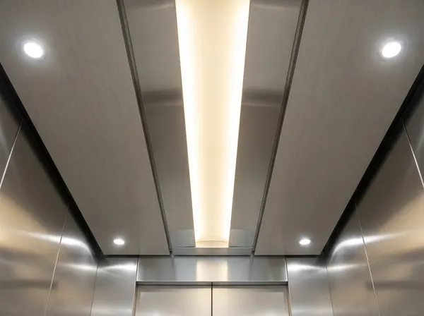 Modern lift cab with integrated LED edge-lit ceiling panel and downlights, replacing original fluorescent lighting